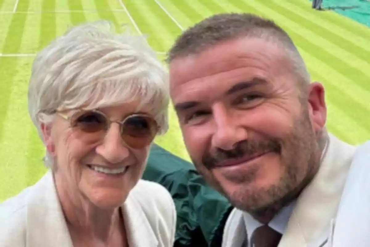 David Beckham and his mother smile as they take a selfie on a well-manicured grass field. David Beckham and his mother smile as they take a selfie on a well-manicured grass field.
