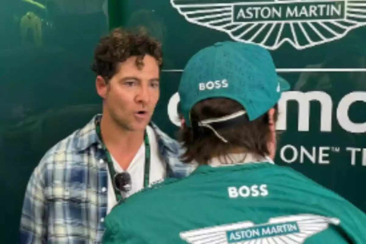 Dues persones conversen davant d’un fons verd amb el logotip d’Aston Martin, una d’elles és Fernando Alonso i porta roba i gorra verda amb la paraula Boss i l’altra, que és David Bisbal, porta una camisa de quadres. Dues persones conversen davant d’un fons verd amb el logotip d’Aston Martin, una d’elles és Fernando Alonso i porta roba i gorra verda amb la paraula Boss i l’altra, que és David Bisbal, porta una camisa de quadres.