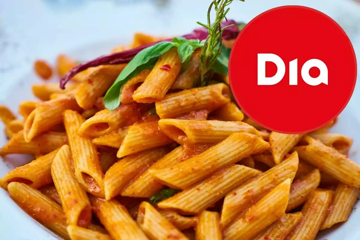 Plat de pasta penne amb salsa de tomàquet i fulles d’alfàbrega amb un logotip vermell de la marca Dia a la cantonada superior dreta Plat de pasta penne amb salsa de tomàquet i fulles d’alfàbrega amb un logotip vermell de la marca Dia a la cantonada superior dreta