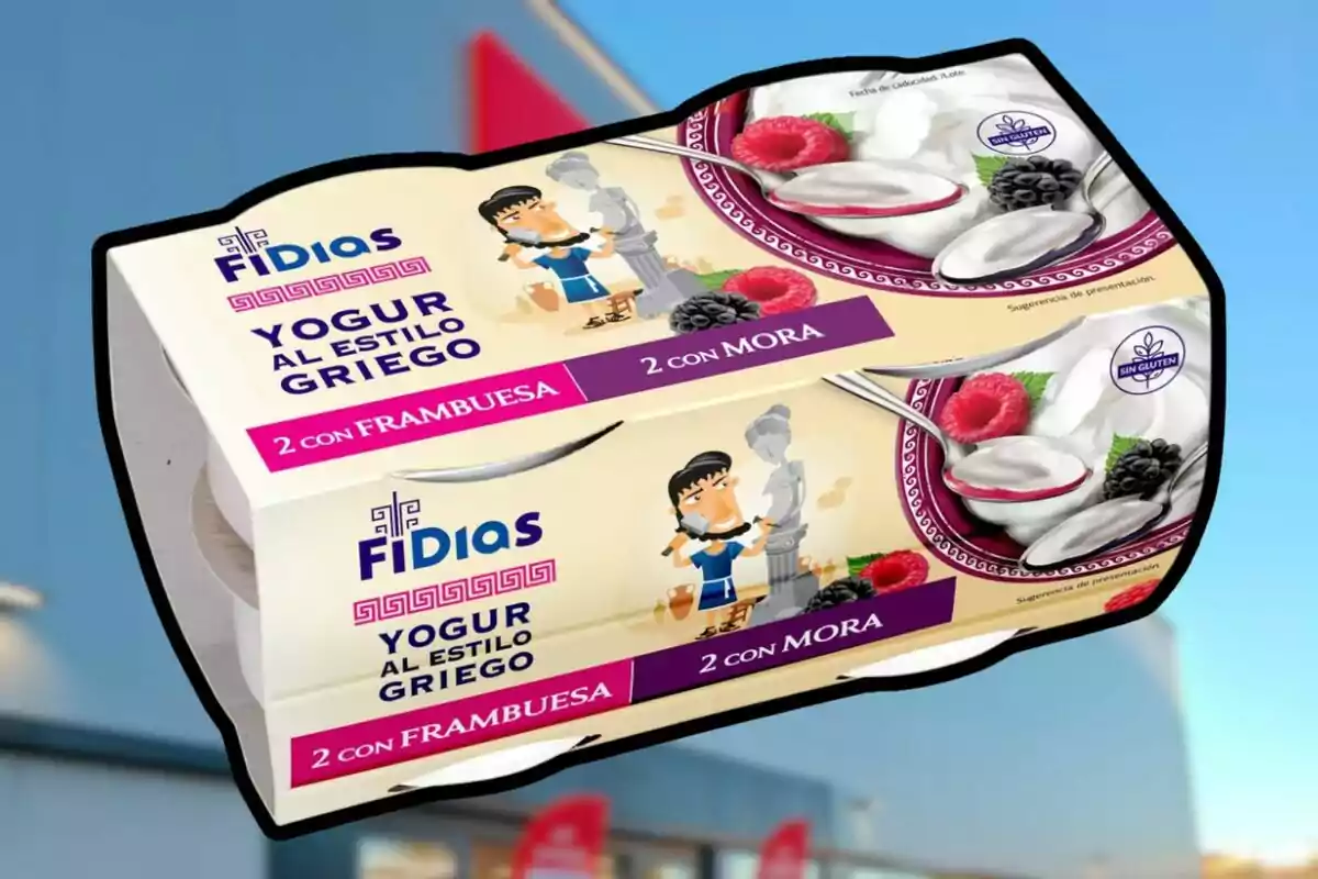 Paquete de yogur al estilo griego marca Fidias con sabores de frambuesa y mora, ilustrado con una caricatura de escultor griego y una estatua, sobre un fondo desenfocado de edificio azul Paquete de yogur al estilo griego marca Fidias con sabores de frambuesa y mora, ilustrado con una caricatura de escultor griego y una estatua, sobre un fondo desenfocado de edificio azul