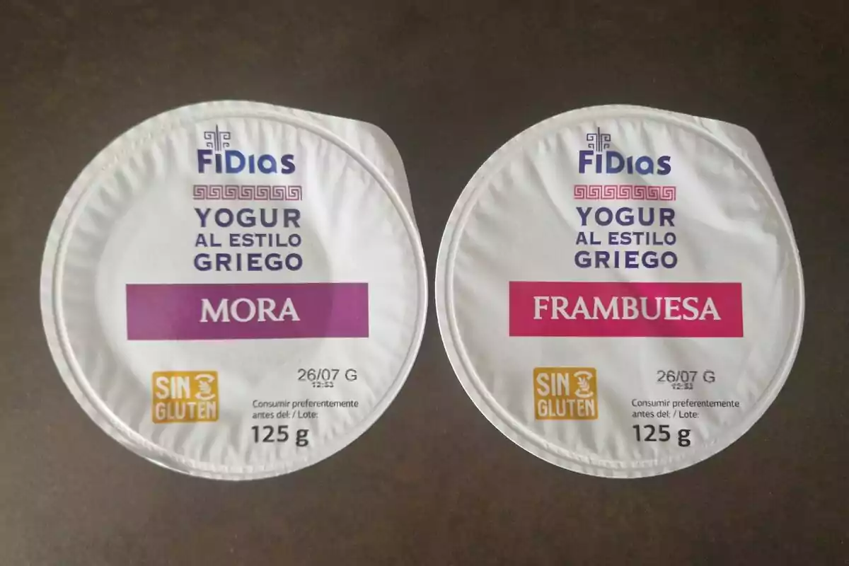 Dos envases de yogur griego marca Fidias, uno de sabor mora y otro de frambuesa, ambos sin gluten y de 125 gramos cada uno, sobre una superficie oscura Dos envases de yogur griego marca Fidias, uno de sabor mora y otro de frambuesa, ambos sin gluten y de 125 gramos cada uno, sobre una superficie oscura