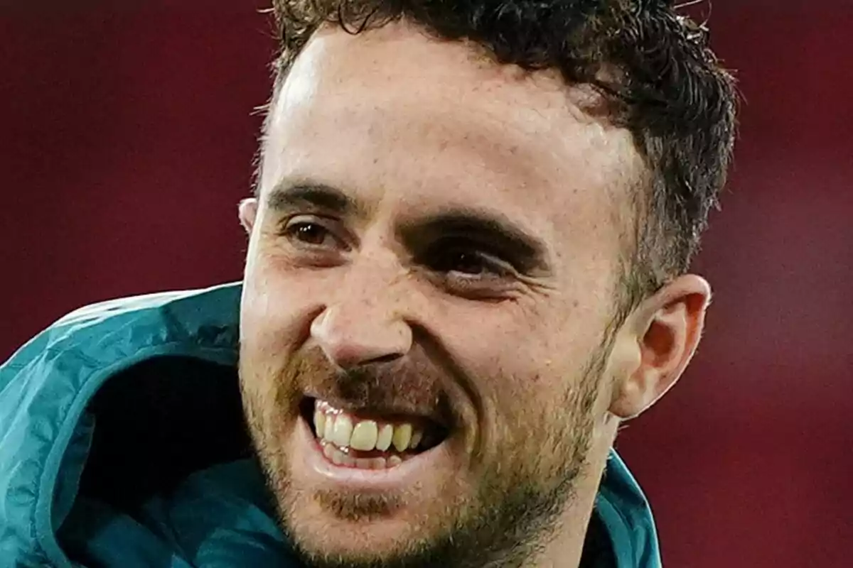 Diogo Jota con barba corta y cabello rizado sonriendo mientras lleva una chaqueta deportiva verde. Diogo Jota con barba corta y cabello rizado sonriendo mientras lleva una chaqueta deportiva verde.