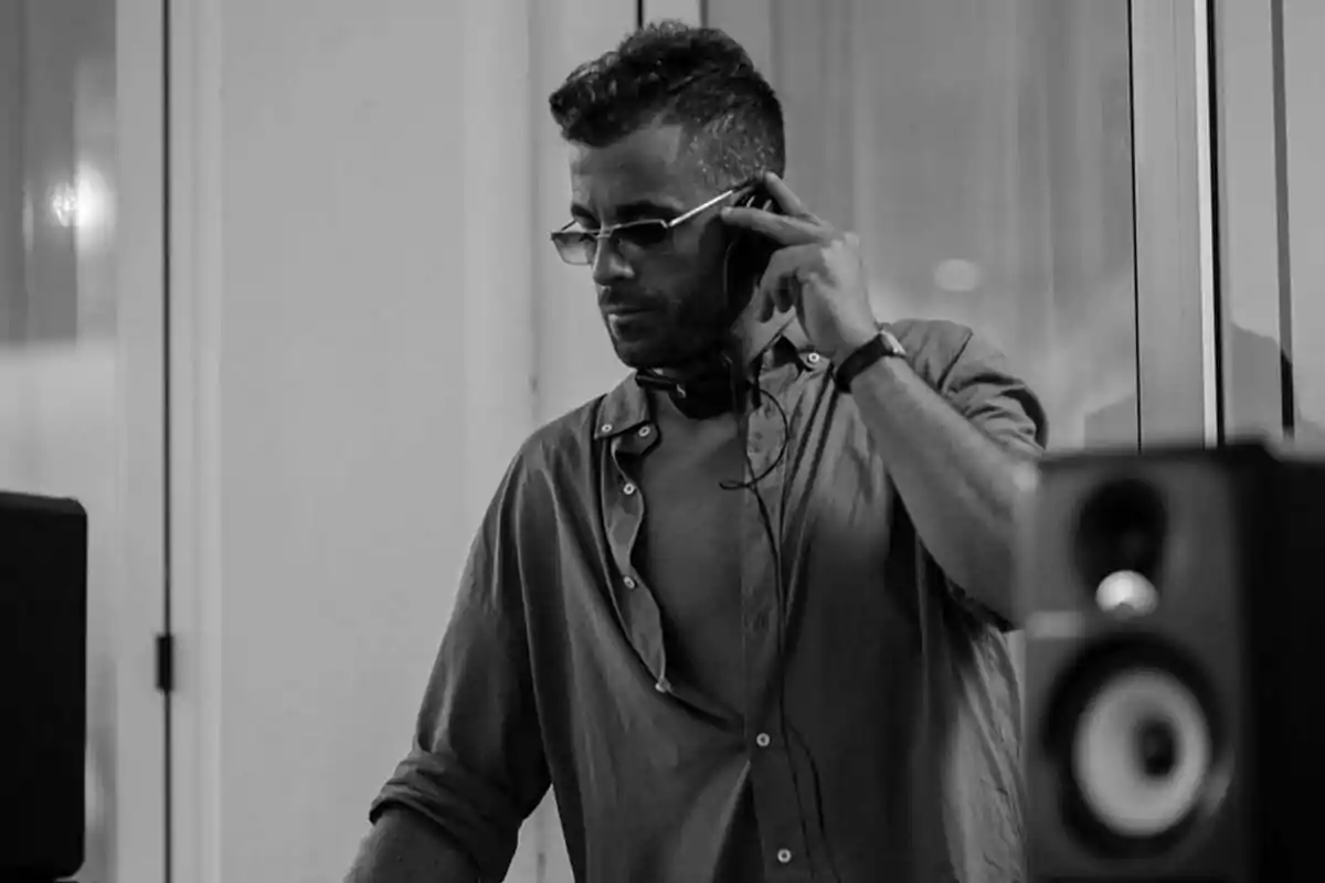 Man with glasses and an unbuttoned jersey wearing headphones while mixing music in a DJ booth in black and white Man with glasses and an unbuttoned jersey wearing headphones while mixing music in a DJ booth in black and white