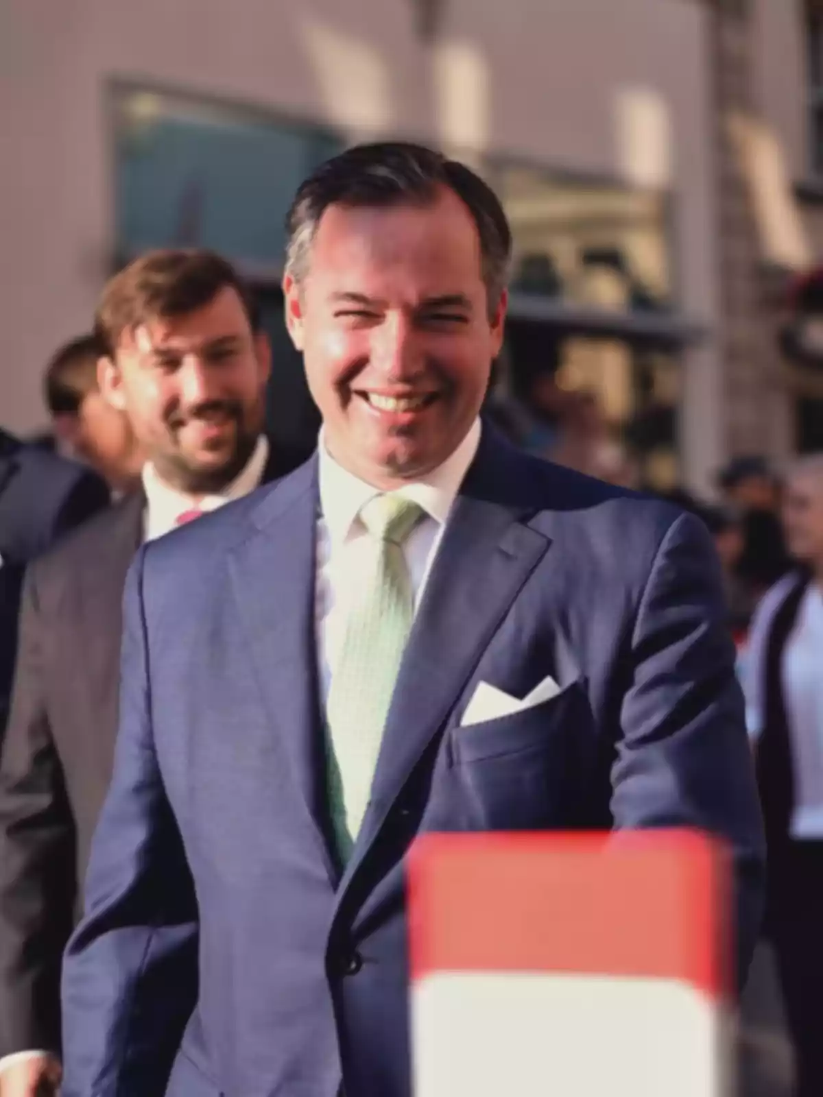 Home somrient amb vestit blau i corbata verd clar caminant a l’aire lliure en un esdeveniment formal Home somrient amb vestit blau i corbata verd clar caminant a l’aire lliure en un esdeveniment formal