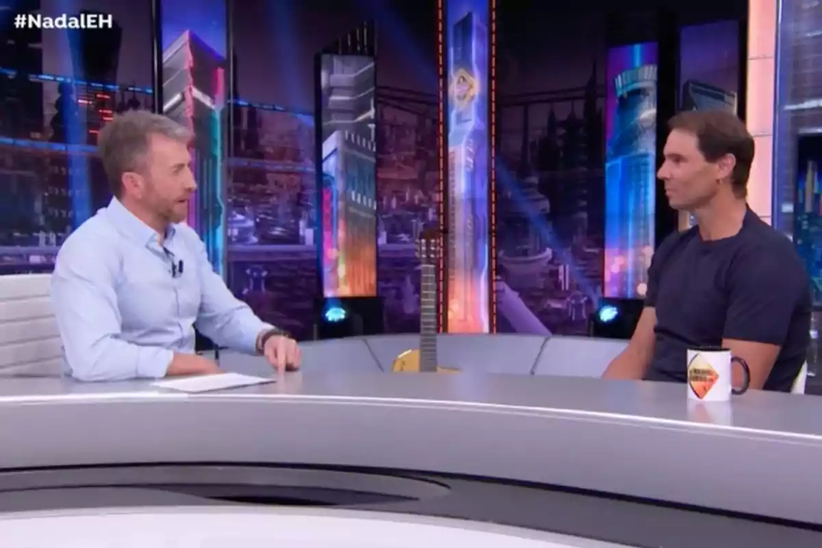 Pablo Motos i Rafa Nadal conversen asseguts en un plató de televisió modern amb llums de colors i una guitarra recolzada a la taula. Captura d’‘El Hormiguero’ Pablo Motos i Rafa Nadal conversen asseguts en un plató de televisió modern amb llums de colors i una guitarra recolzada a la taula. Captura d’‘El Hormiguero’