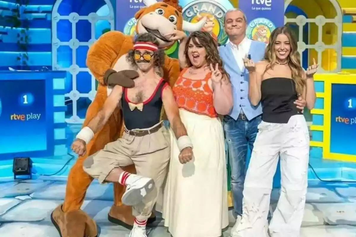 Cinc persones posen somrients en un plató de televisió colorit, una d’elles porta una disfressa de toro i l’ambient és alegre i divertit. Cinc persones posen somrients en un plató de televisió colorit, una d’elles porta una disfressa de toro i l’ambient és alegre i divertit.