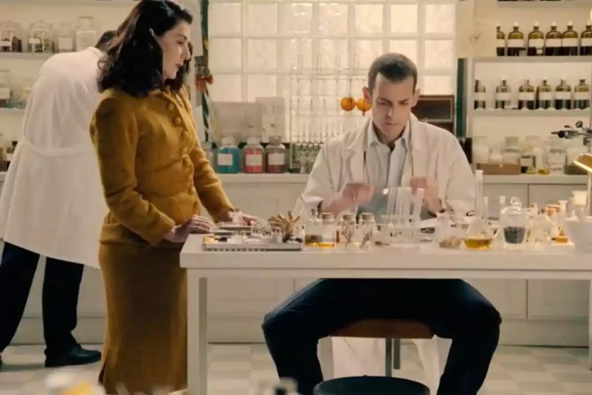 Dues persones en un laboratori envoltades de flascons i material científic mentre una treballa a la taula i l’altra observa en una escena de 'Sueños de Libertad'. Dues persones en un laboratori envoltades de flascons i material científic mentre una treballa a la taula i l’altra observa en una escena de 'Sueños de Libertad'.