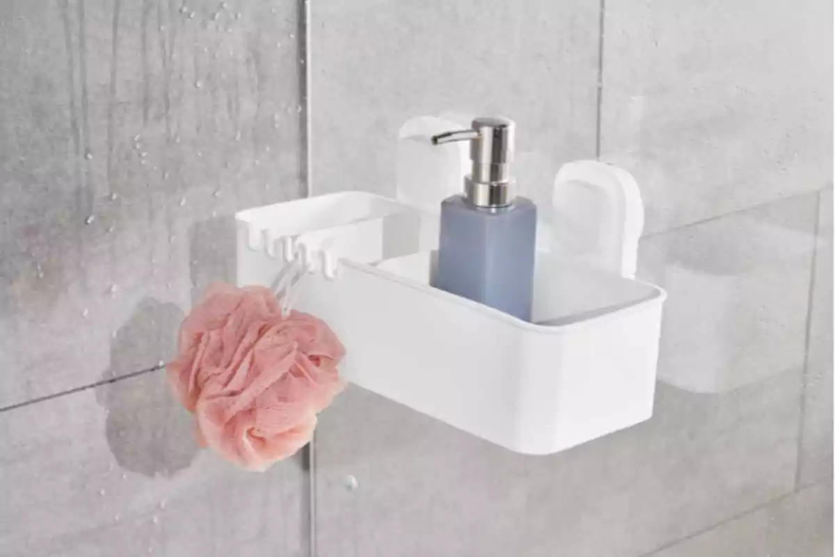 Organitzador blanc de bany adherit a una paret de vidre amb una esponja de bany rosa penjada i un dispensador de sabó líquid blau. Organitzador blanc de bany adherit a una paret de vidre amb una esponja de bany rosa penjada i un dispensador de sabó líquid blau.