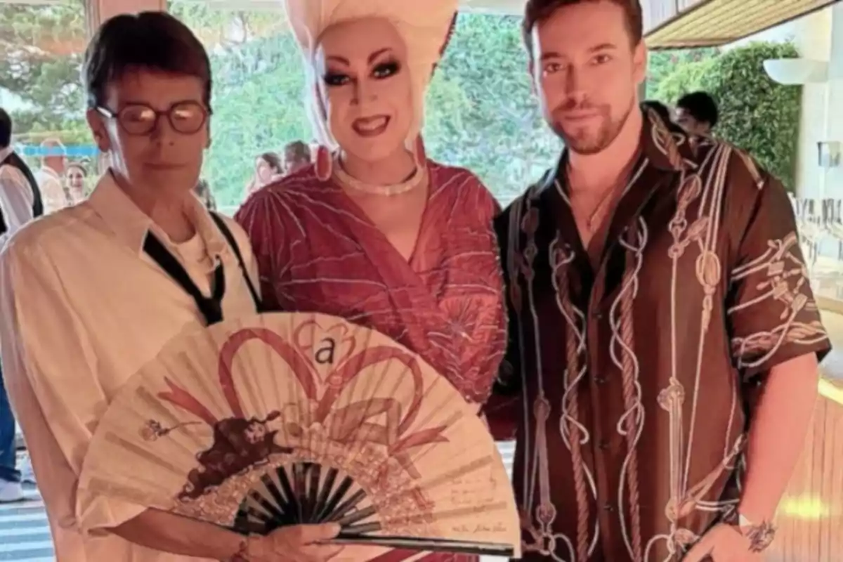 Tres persones posen juntes en un esdeveniment social, una d’elles sosté un ventall decorat i una altra porta un pentinat elaborat i un maquillatge cridaner. Tres persones posen juntes en un esdeveniment social, una d’elles sosté un ventall decorat i una altra porta un pentinat elaborat i un maquillatge cridaner.