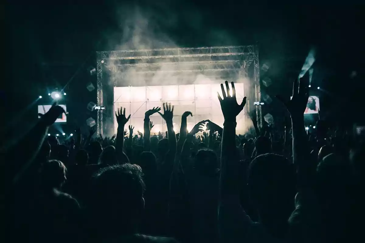 Persones aixecant les mans i gaudint d’un concert amb llums brillants a l’escenari