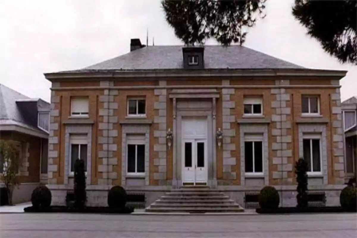 Facade of a brick building with stone details, white main door, and front stairs surrounded by shrubs and trees Facade of a brick building with stone details, white main door, and front stairs surrounded by shrubs and trees