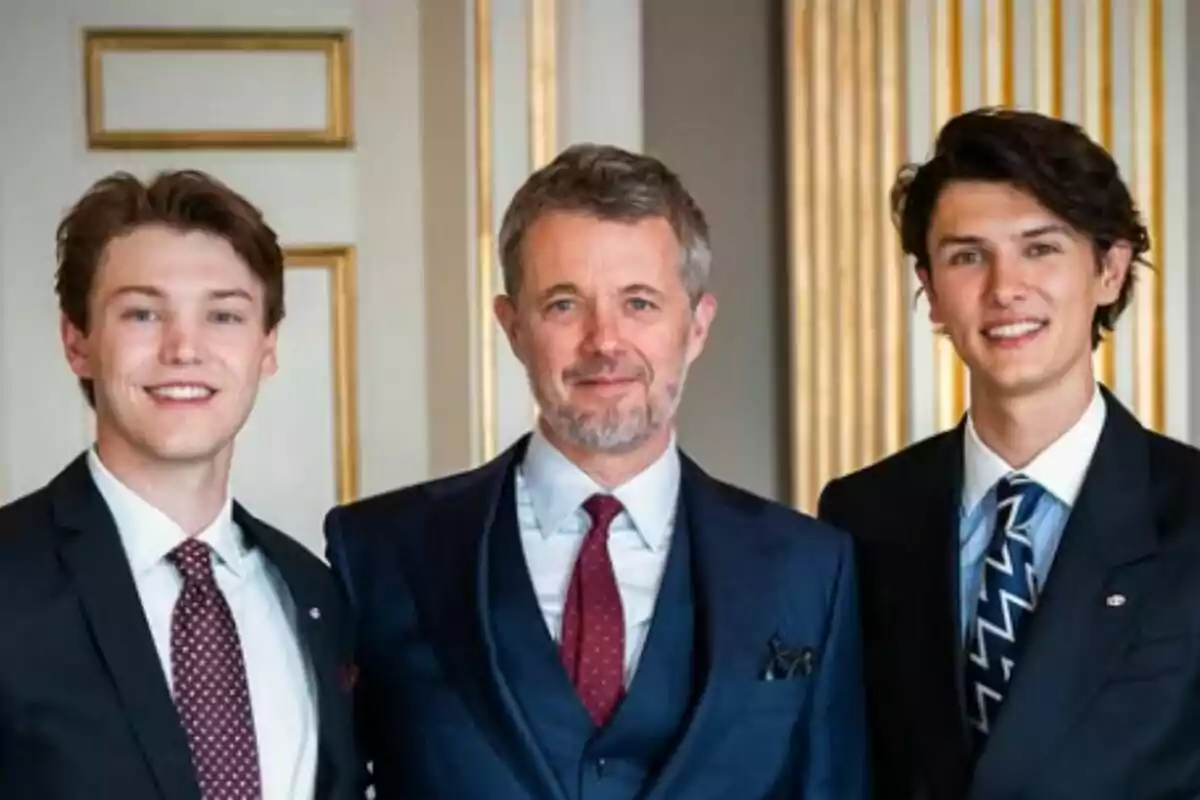 Tres hombres vestidos con traje posan juntos y sonríen en un entorno elegante con detalles dorados en la pared, los tres son Federico, Félix y Nicolás de Dinamarca. Tres hombres vestidos con traje posan juntos y sonríen en un entorno elegante con detalles dorados en la pared, los tres son Federico, Félix y Nicolás de Dinamarca.