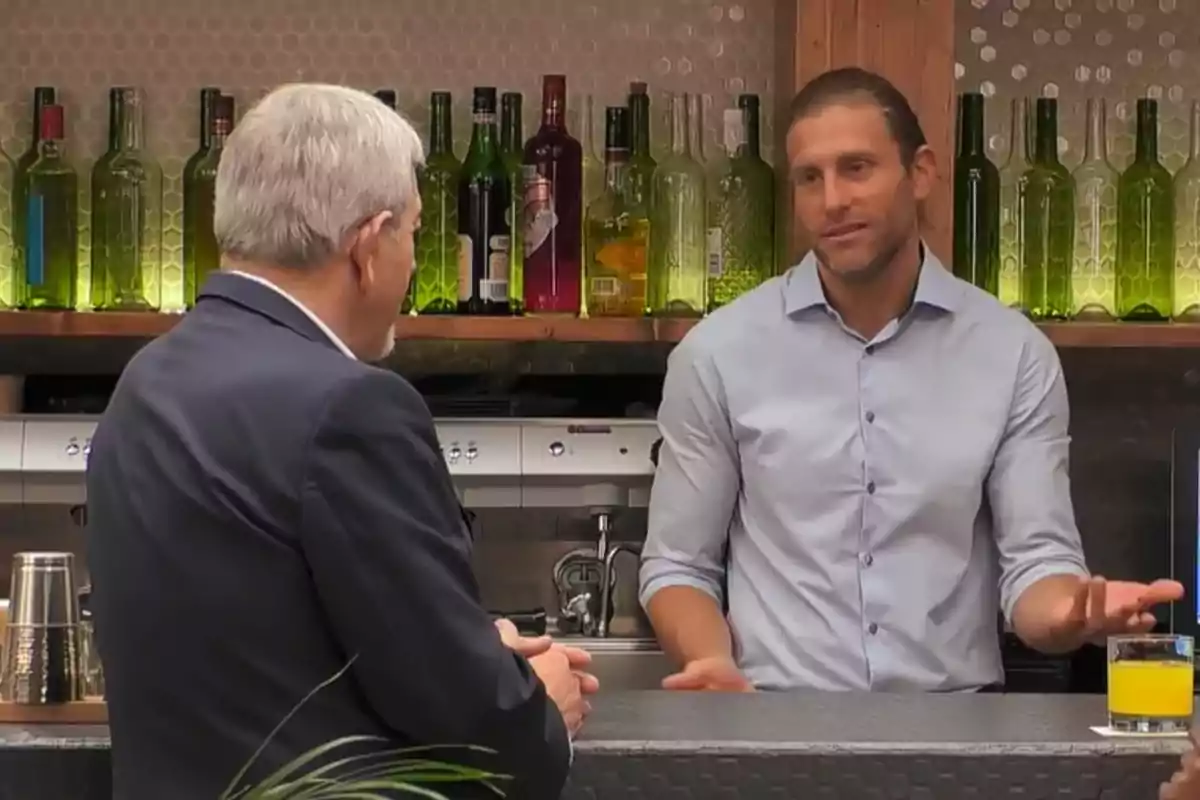 Carlos Sobera i Matías Roure conversen en una barra de bar amb ampolles de vidre al fons i un got amb beguda groga sobre la barra. Captura de 'First Dates' Carlos Sobera i Matías Roure conversen en una barra de bar amb ampolles de vidre al fons i un got amb beguda groga sobre la barra. Captura de 'First Dates'