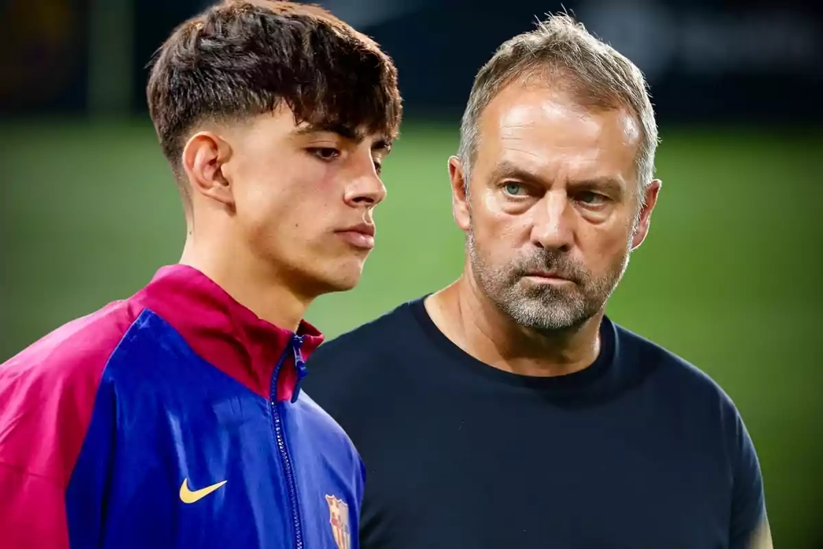 Two people in the foreground, one wearing a Barcelona sports jacket and the other in a dark jersey, both with serious expressions in a soccer field setting.
