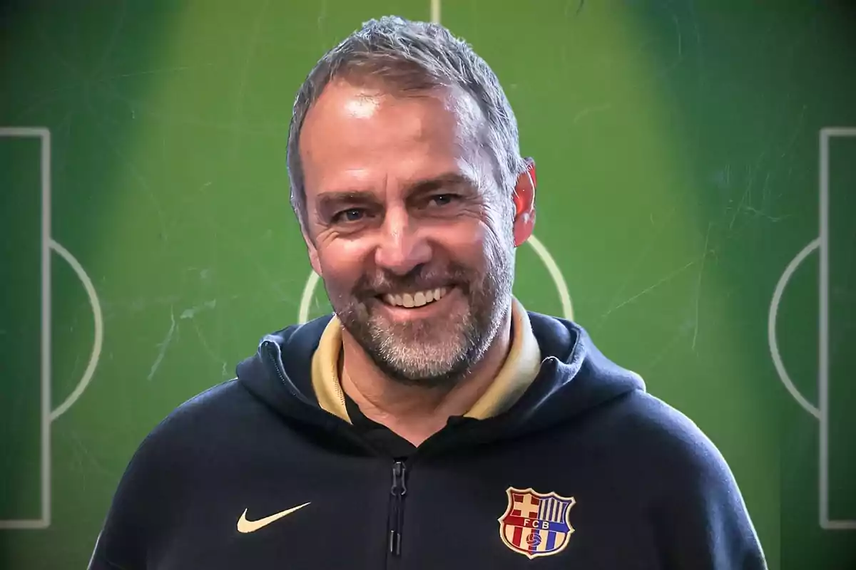 Home somrient amb barba i dessuadora del FC Barcelona davant d’un fons de camp de futbol