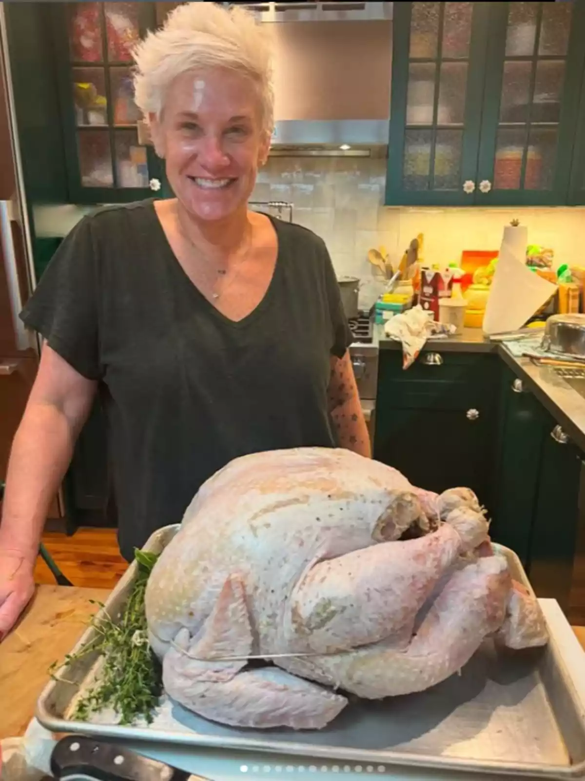 Anne Burrell sonriente en una cocina junto a un pavo crudo preparado en una bandeja para hornear