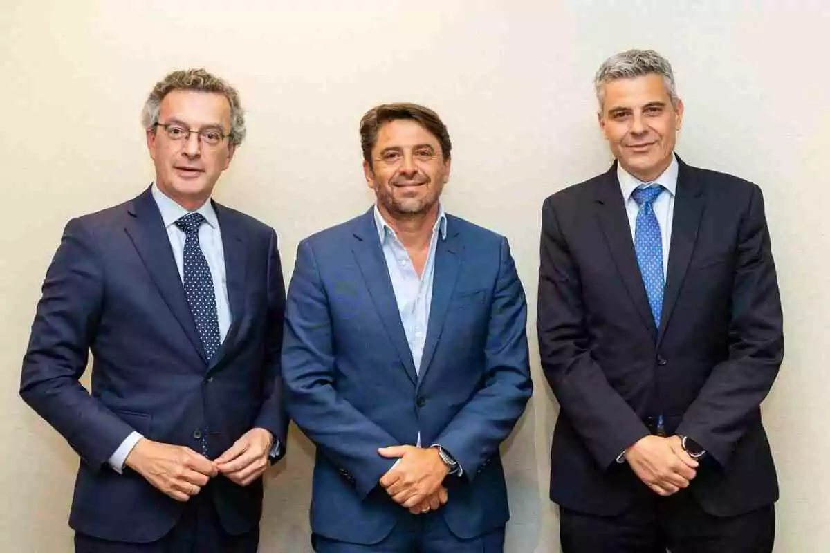 Tres homes vestits amb vestit posen junts davant d’una paret clara Tres homes vestits amb vestit posen junts davant d’una paret clara