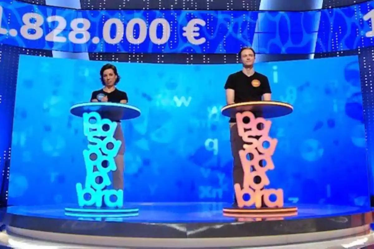 Rosa i Manu drets a 'Pasapalabra' amb temàtica blava i taronja, cadascun darrere d’un faristol amb la paraula pasapalabra formada per lletres grans i acolorides, i una pantalla al fons mostrant una quantitat de diners en euros. Rosa i Manu drets a 'Pasapalabra' amb temàtica blava i taronja, cadascun darrere d’un faristol amb la paraula pasapalabra formada per lletres grans i acolorides, i una pantalla al fons mostrant una quantitat de diners en euros.