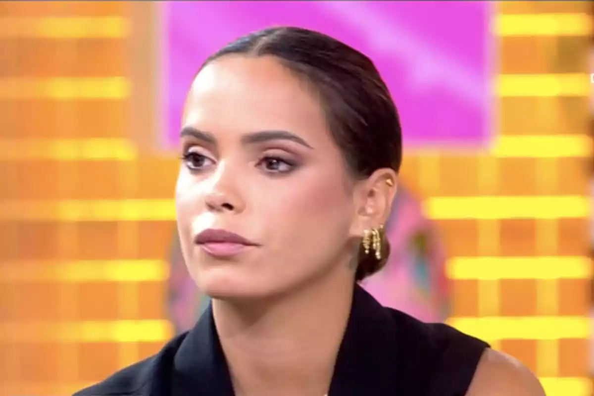 Gloria Camila de cabello oscuro recogido con expresión seria en un set de televisión con fondo colorido Gloria Camila de cabello oscuro recogido con expresión seria en un set de televisión con fondo colorido