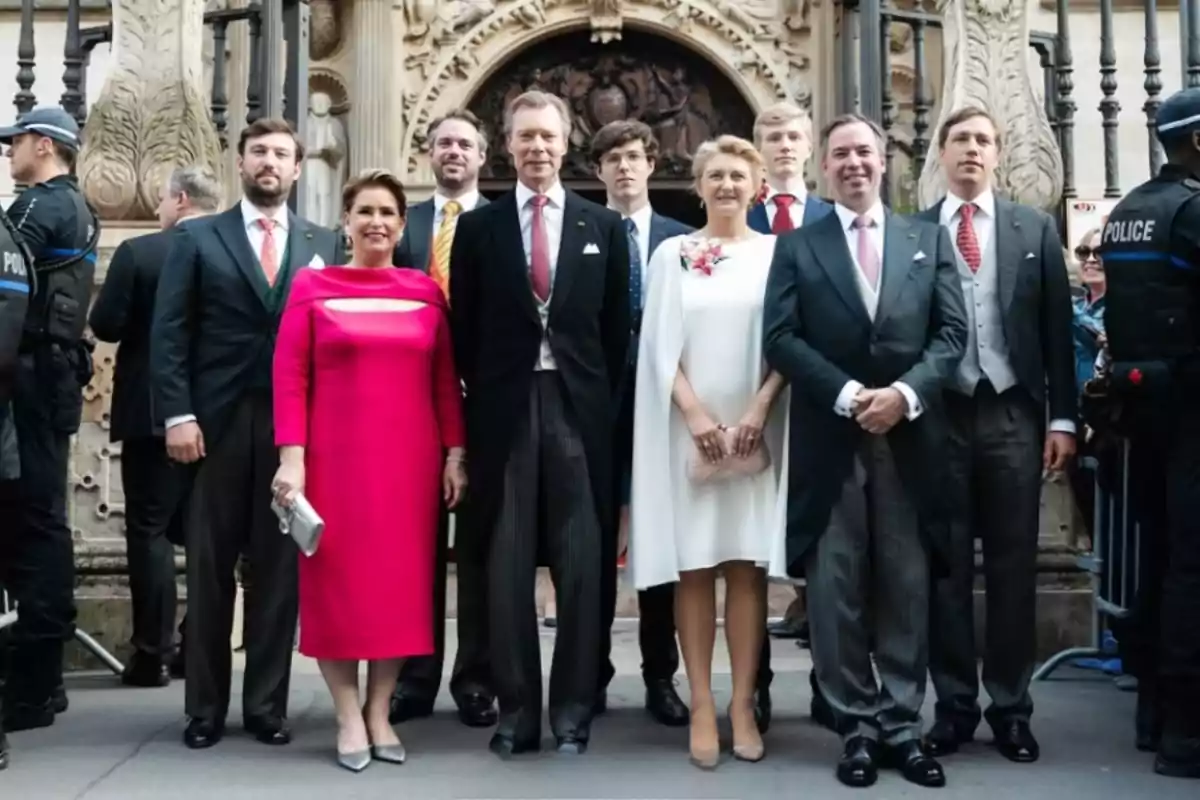 Un grup de persones elegantment vestides posa davant d’un edifici històric amb detalls arquitectònics decoratius i presència de policies als costats. Un grup de persones elegantment vestides posa davant d’un edifici històric amb detalls arquitectònics decoratius i presència de policies als costats.