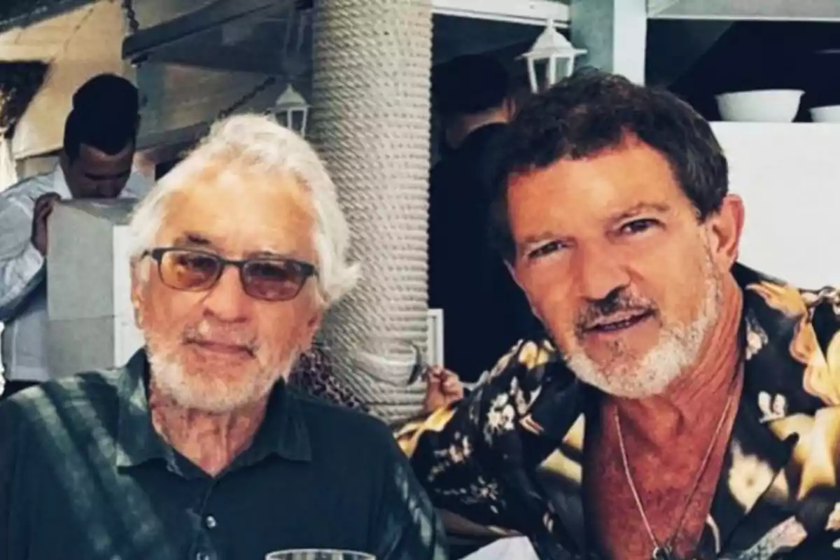 Antonio Banderas y Robert de Niro mayores posan juntos en un restaurante, ambos con barba y cabello canoso, uno lleva gafas y el otro una camisa estampada. Antonio Banderas y Robert de Niro mayores posan juntos en un restaurante, ambos con barba y cabello canoso, uno lleva gafas y el otro una camisa estampada.