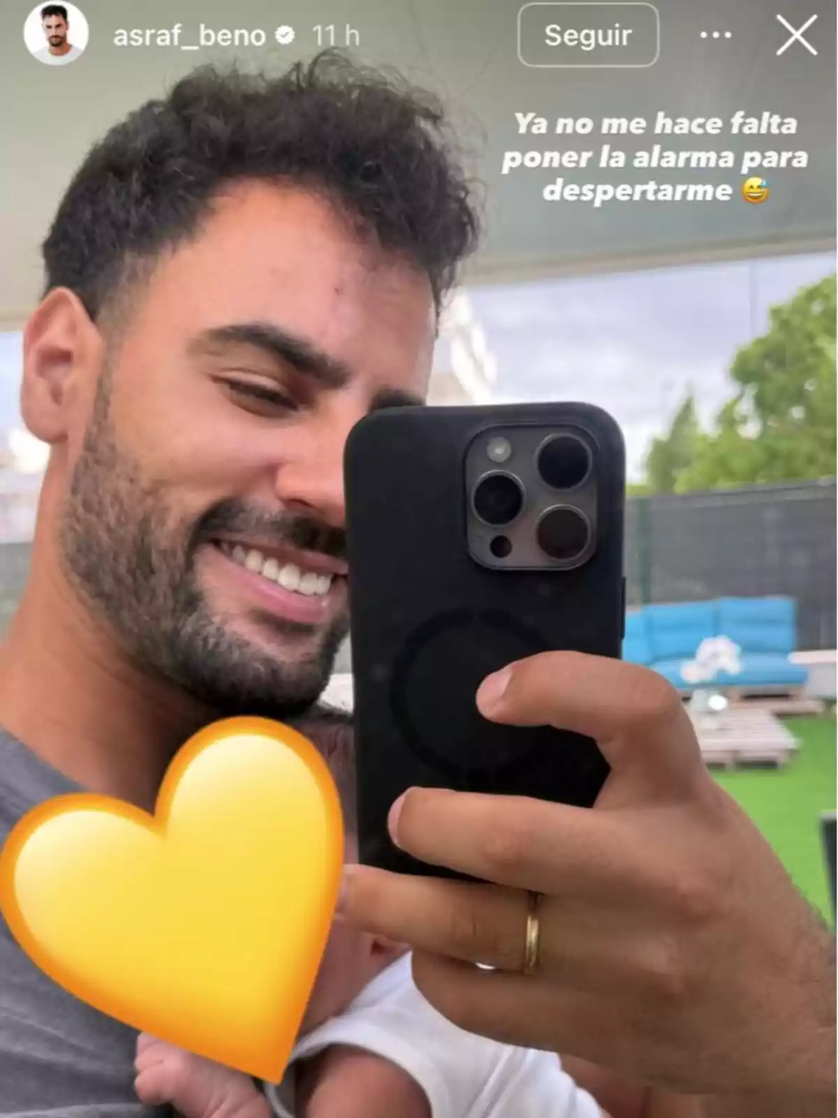 Home somrient fent-se una selfie amb un nadó als braços parcialment cobert per un emoji de cor groc Home somrient fent-se una selfie amb un nadó als braços parcialment cobert per un emoji de cor groc