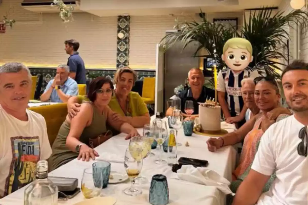 Grup de persones assegudes al voltant d’una taula en un restaurant celebrant amb un pastís i un emoji cobrint la cara d’un nen Grup de persones assegudes al voltant d’una taula en un restaurant celebrant amb un pastís i un emoji cobrint la cara d’un nen