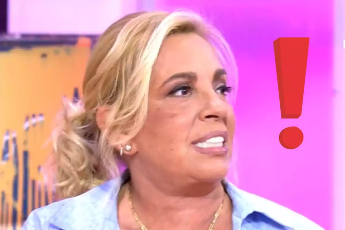 Carmen Borrego rubia mirando hacia un lado con un gran signo de exclamación rojo junto a su rostro sobre un fondo rosa