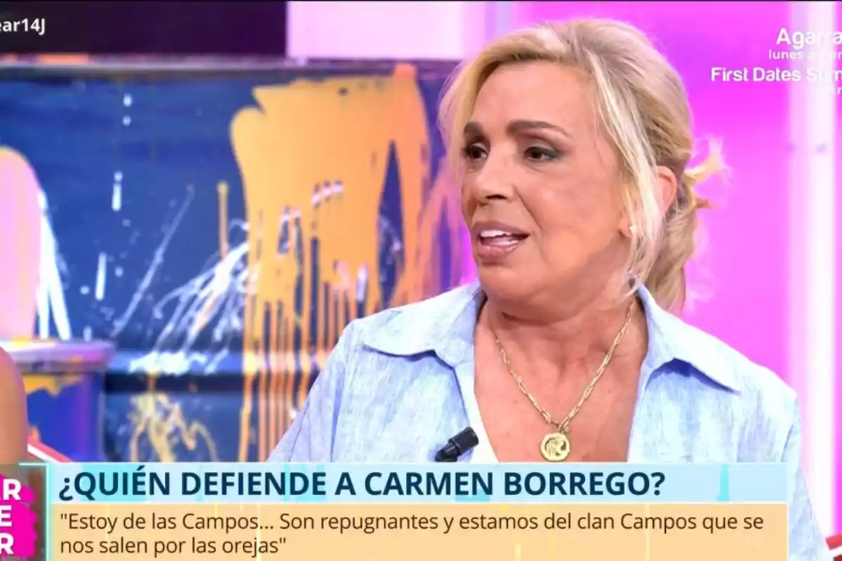 Dona rossa amb camisa blau clar i collaret daurat parlant en un programa de televisió amb un rètol que pregunta qui defensa Carmen Borrego i un fons acolorit Dona rossa amb camisa blau clar i collaret daurat parlant en un programa de televisió amb un rètol que pregunta qui defensa Carmen Borrego i un fons acolorit