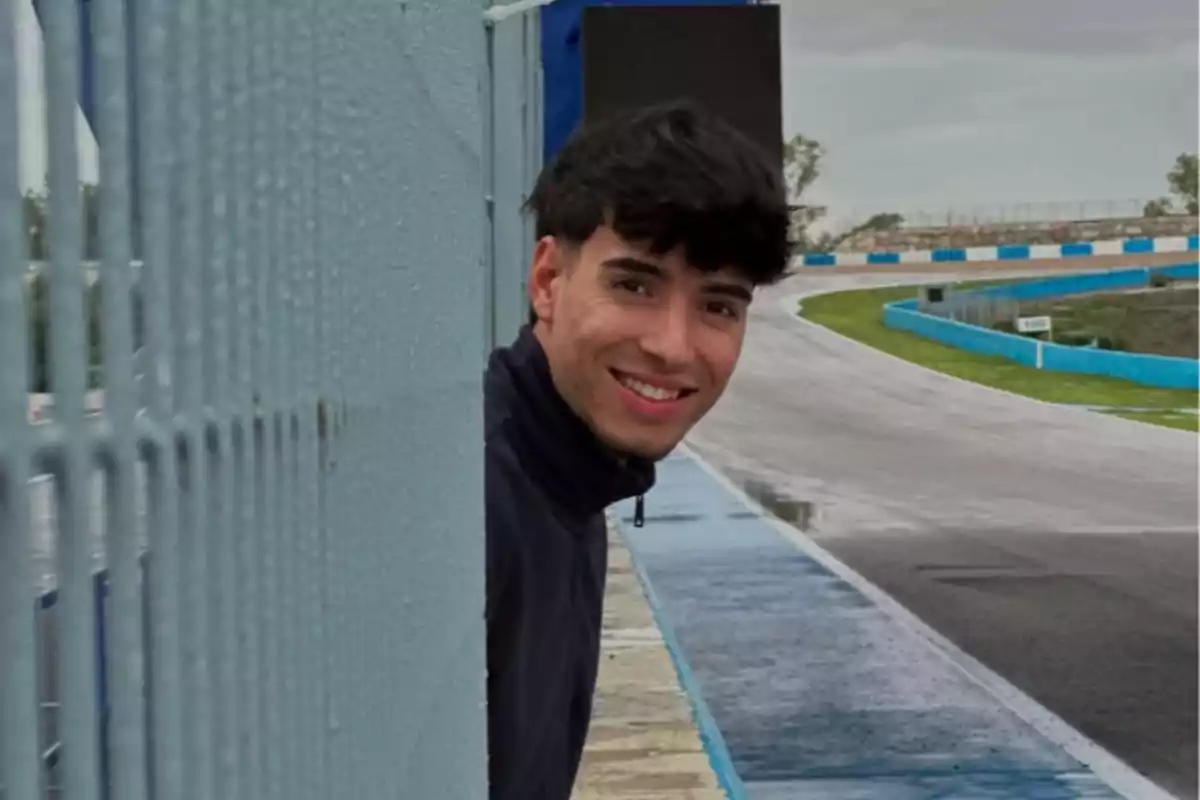 Borja Gómez sonriendo asomado detrás de una valla en un circuito de carreras mojado Borja Gómez sonriendo asomado detrás de una valla en un circuito de carreras mojado