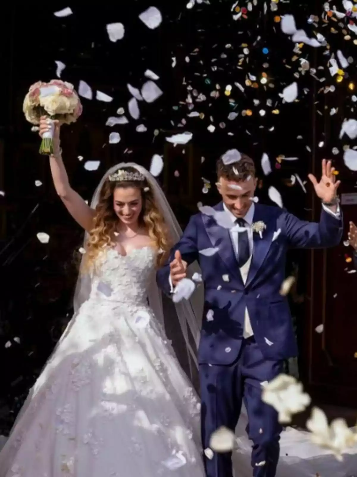 Newlywed couple leaving a church while flower petals are being thrown at them; the bride is wearing a white dress and holding a bouquet, and the groom, who is Diogo Jota, is dressed in a blue suit. Newlywed couple leaving a church while flower petals are being thrown at them; the bride is wearing a white dress and holding a bouquet, and the groom, who is Diogo Jota, is dressed in a blue suit.