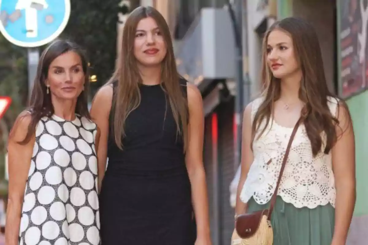 La reina Letizia, la infanta Sofía y la princesa Leonor jóvenes posan juntas en una calle, luciendo ropa veraniega y sonriendo suavemente La reina Letizia, la infanta Sofía y la princesa Leonor jóvenes posan juntas en una calle, luciendo ropa veraniega y sonriendo suavemente
