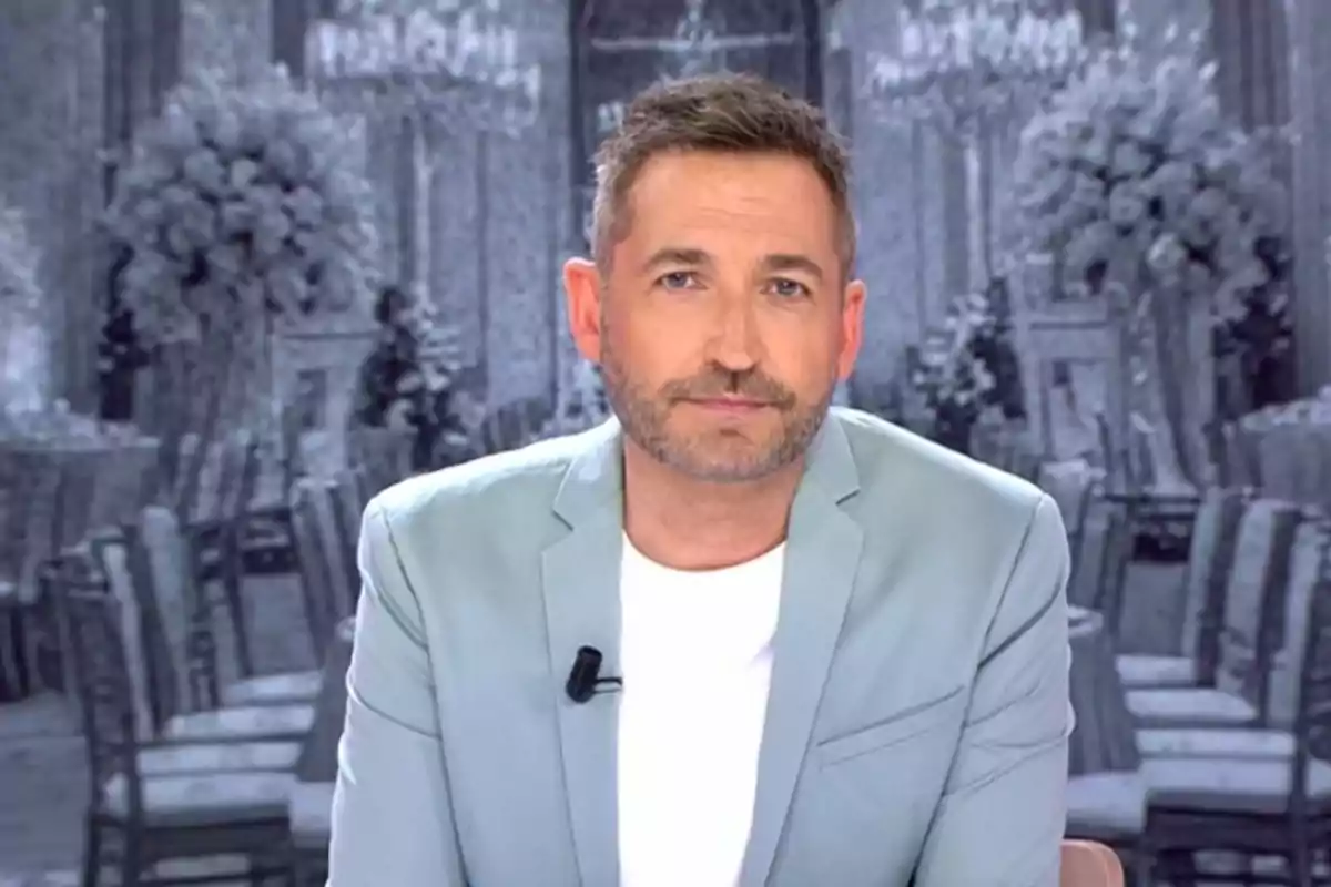 Frank Blanco de cabello corto y barba con chaqueta clara y camiseta blanca sentado frente a un fondo elegante en tonos grises Frank Blanco de cabello corto y barba con chaqueta clara y camiseta blanca sentado frente a un fondo elegante en tonos grises