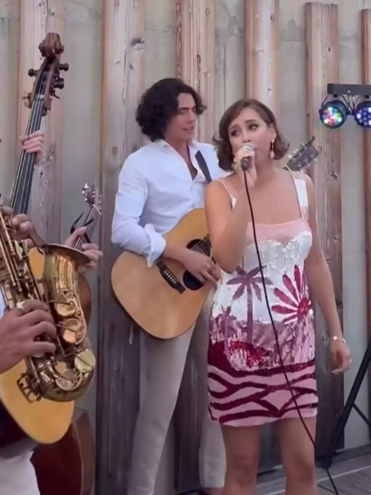 Grup musical tocant a l’aire lliure amb una cantant al davant i músics tocant guitarra, saxòfon i contrabaix, tots vestits de manera elegant. Grup musical tocant a l’aire lliure amb una cantant al davant i músics tocant guitarra, saxòfon i contrabaix, tots vestits de manera elegant.