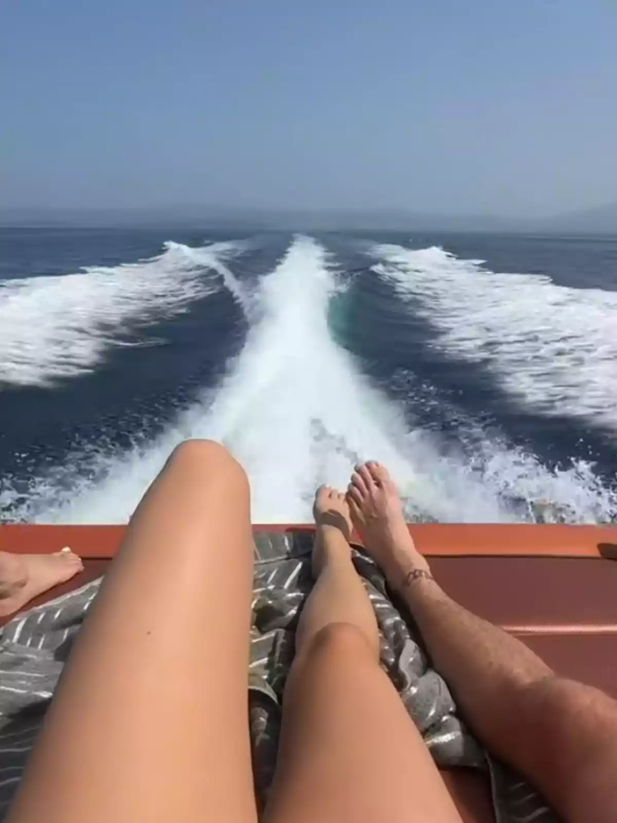 Personas recostadas en la parte trasera de una lancha disfrutando del sol mientras navegan por el mar dejando una estela de agua detrás Personas recostadas en la parte trasera de una lancha disfrutando del sol mientras navegan por el mar dejando una estela de agua detrás