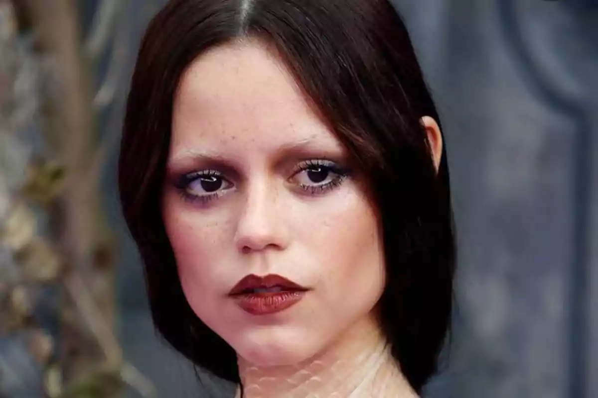 Young woman with dark, straight hair, dramatic makeup, and a serious expression
