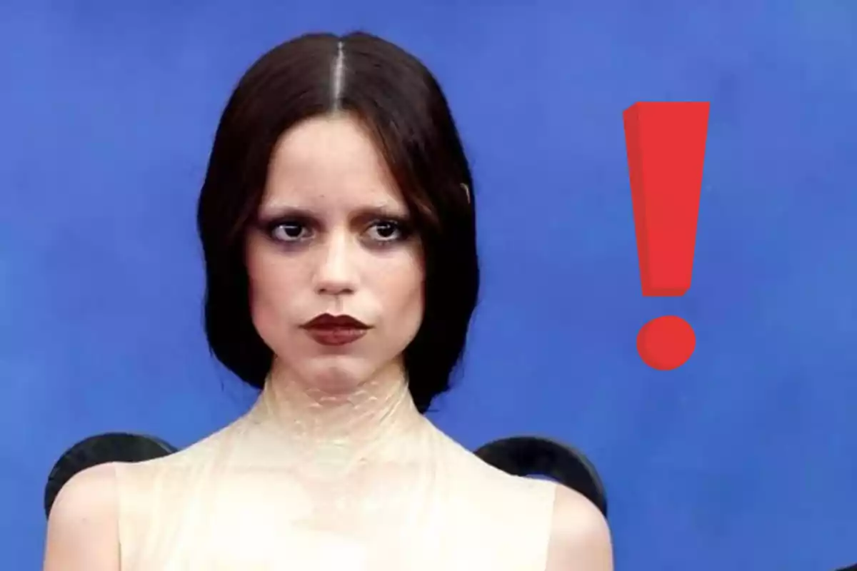 Jenna Ortega de cabello oscuro y expresión seria frente a un fondo azul con un signo de exclamación rojo a su lado