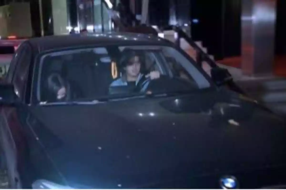 Two people inside a black car parked in front of a building at night
