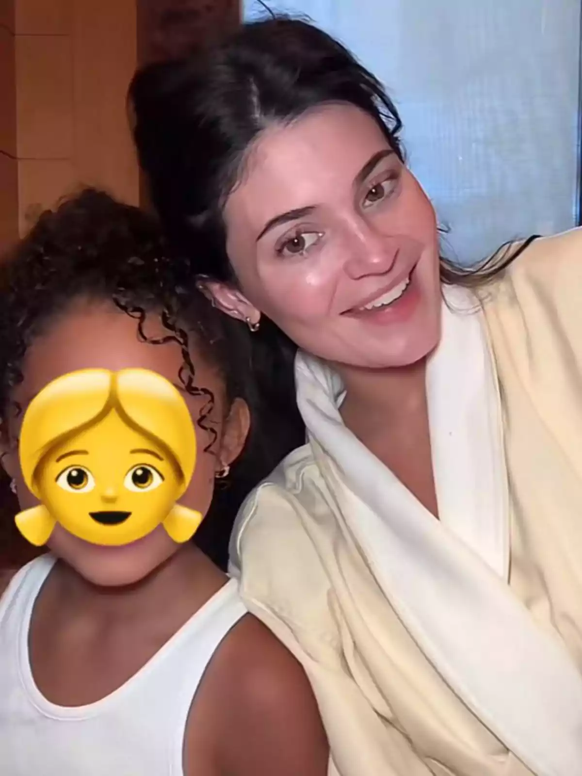 Smiling woman in a light coat next to a girl whose face is covered by a girl emoji Smiling woman in a light coat next to a girl whose face is covered by a girl emoji