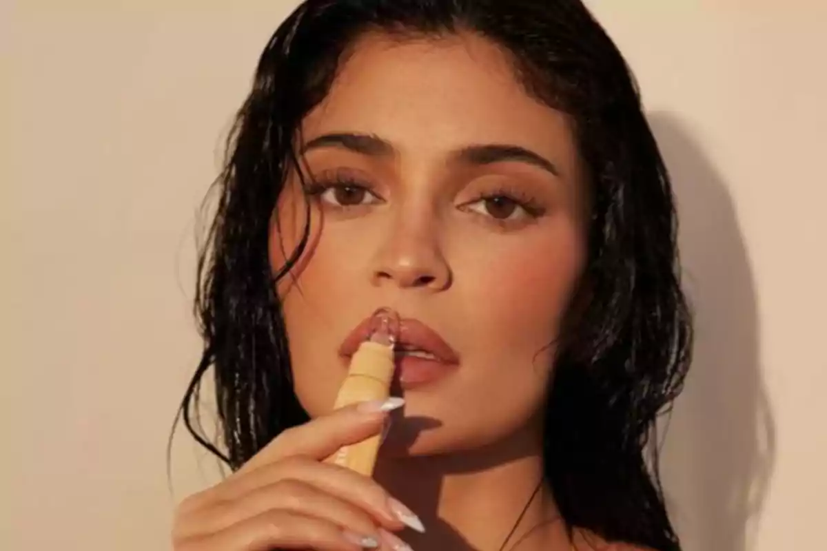 Woman with dark, damp hair applying clear lip gloss to her lips Woman with dark, damp hair applying clear lip gloss to her lips