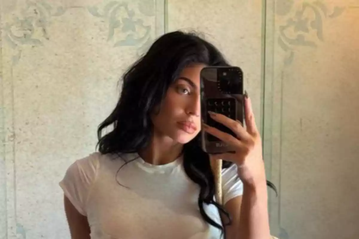Dark-haired woman taking a selfie in front of a mirror wearing a white t-jersey Dark-haired woman taking a selfie in front of a mirror wearing a white t-jersey