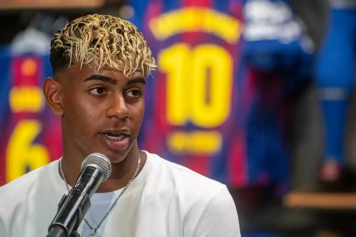 Jove amb cabell ros arrissat parlant davant d’un micròfon amb samarretes de futbol del Barcelona al fons Jove amb cabell ros arrissat parlant davant d’un micròfon amb samarretes de futbol del Barcelona al fons