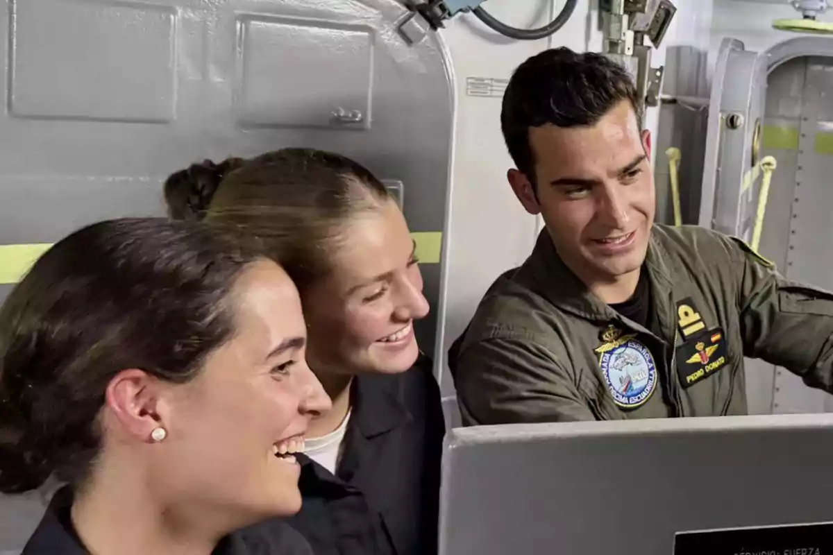 Three young people in military uniforms smile as they look at a screen inside a military vessel or facility. Three young people in military uniforms smile as they look at a screen inside a military vessel or facility.