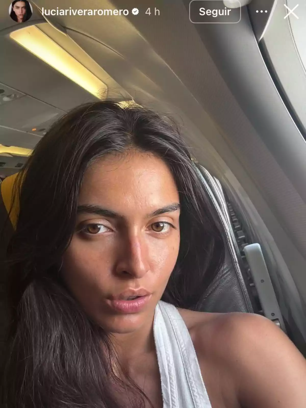 Dona de cabells llargs i foscos asseguda al costat de la finestra d’un avió mirant a la càmera