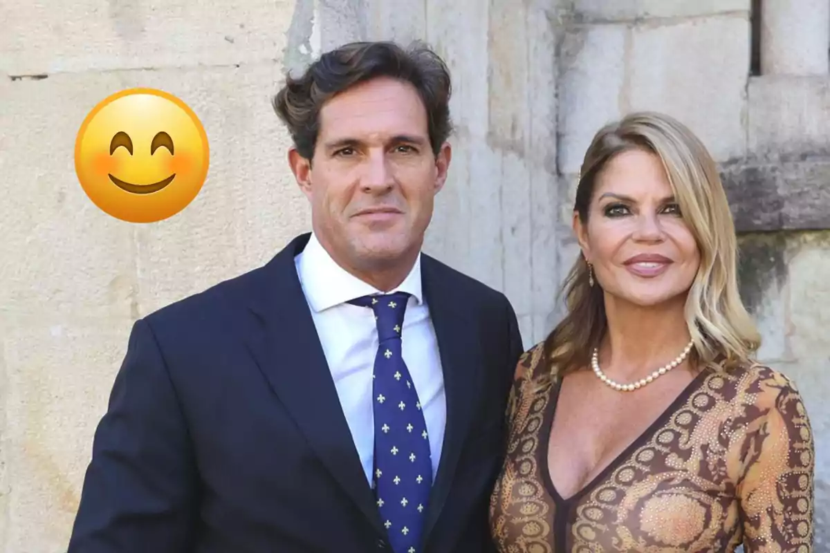 Parella elegantament vestida posant davant d’una paret de pedra amb un gran emoji somrient a l’esquerra Parella elegantament vestida posant davant d’una paret de pedra amb un gran emoji somrient a l’esquerra