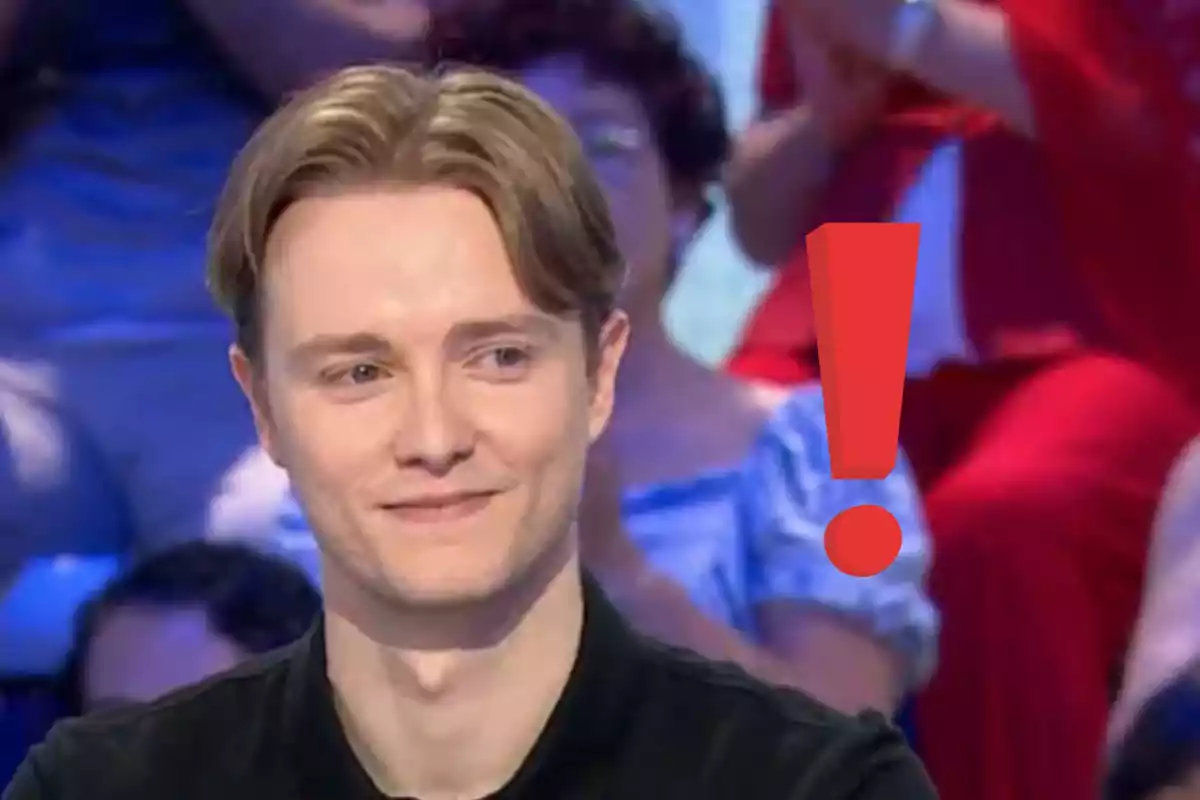 Home jove de cabell ros somrient en un programa de televisió amb un gran signe d’exclamació vermell al seu costat