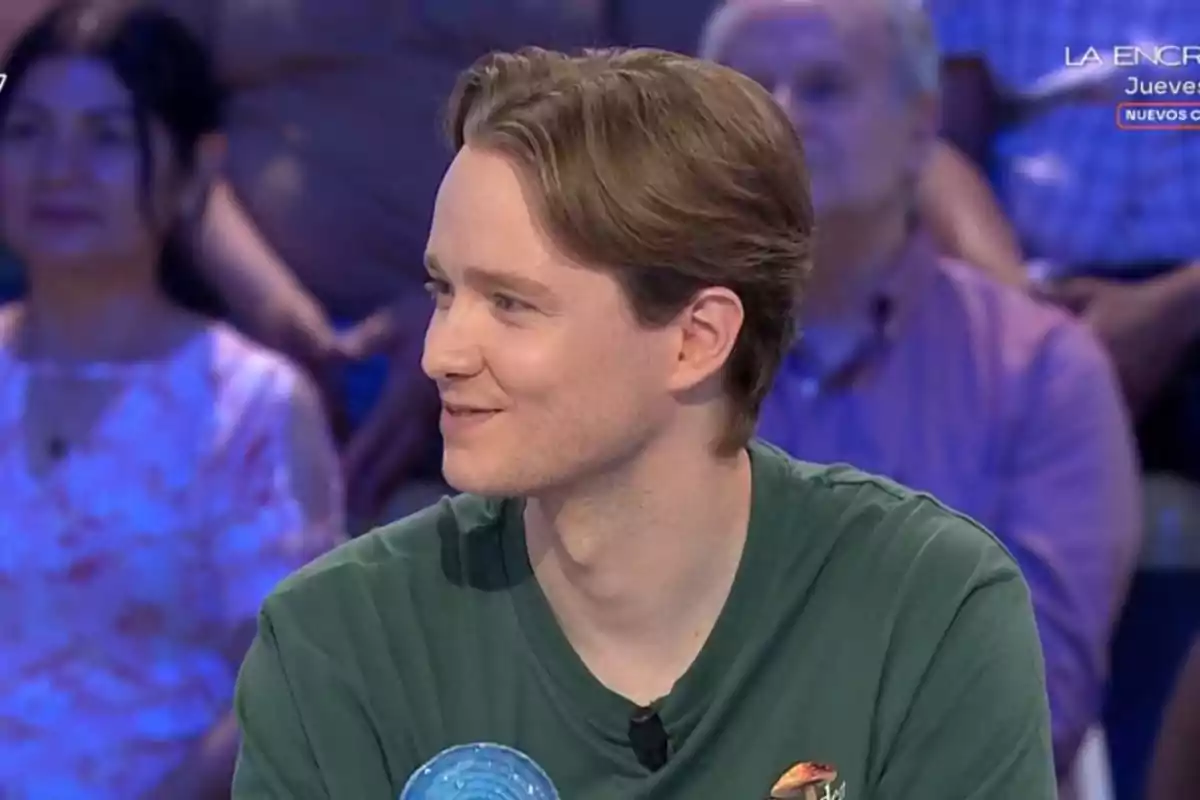 Jove de cabell castany clar i samarreta verda assegut en un programa de televisió amb públic al fons Jove de cabell castany clar i samarreta verda assegut en un programa de televisió amb públic al fons
