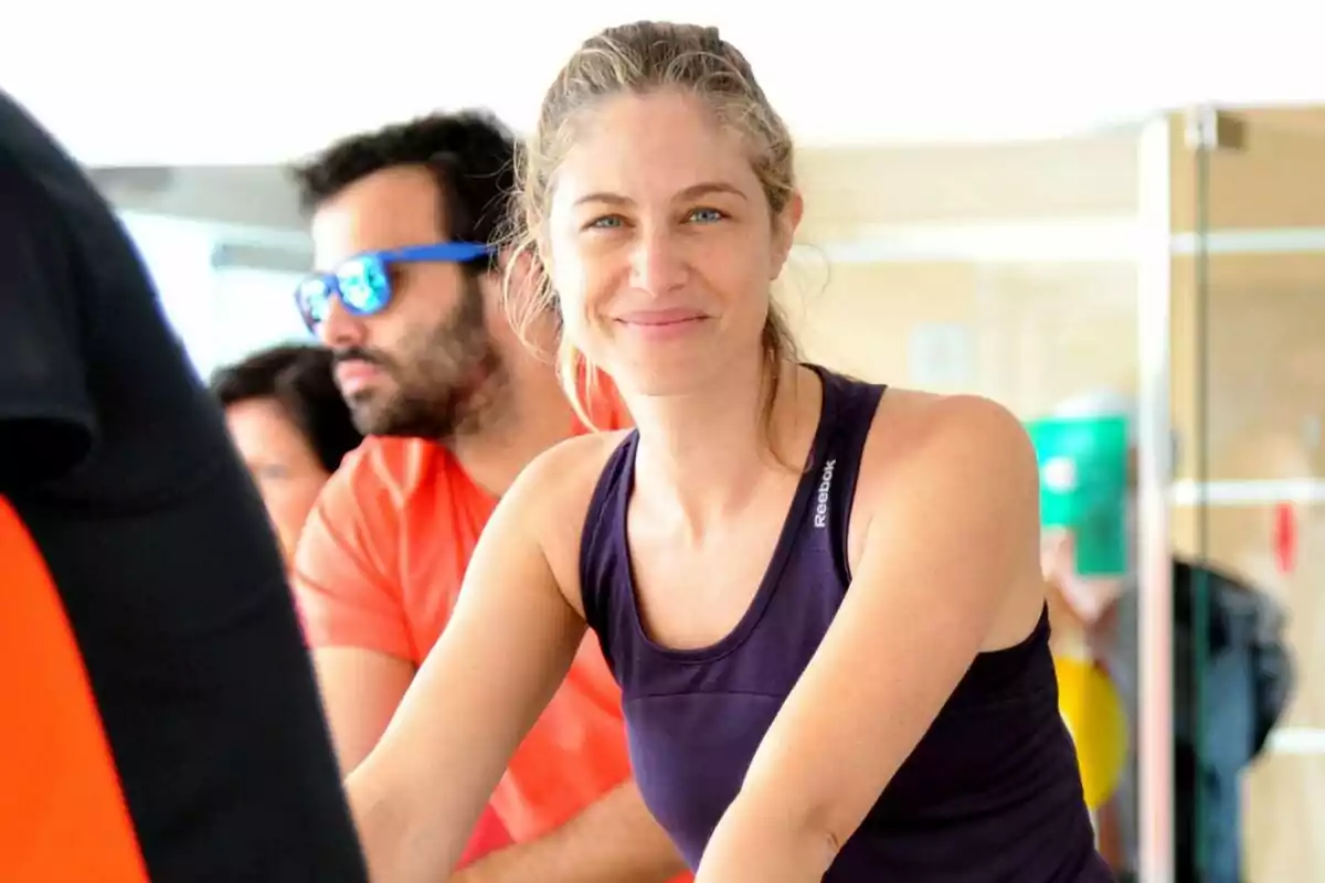 Dona jove amb samarreta esportiva somriu mentre fa exercici en un gimnàs il·luminat Dona jove amb samarreta esportiva somriu mentre fa exercici en un gimnàs il·luminat