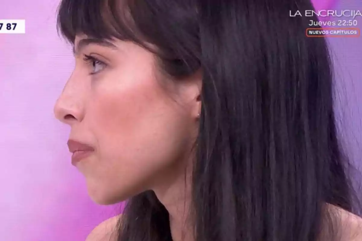 Melani de cabello largo y oscuro vista de perfil en un set de televisión con fondo rosa y texto en la esquina superior derecha Melani de cabello largo y oscuro vista de perfil en un set de televisión con fondo rosa y texto en la esquina superior derecha