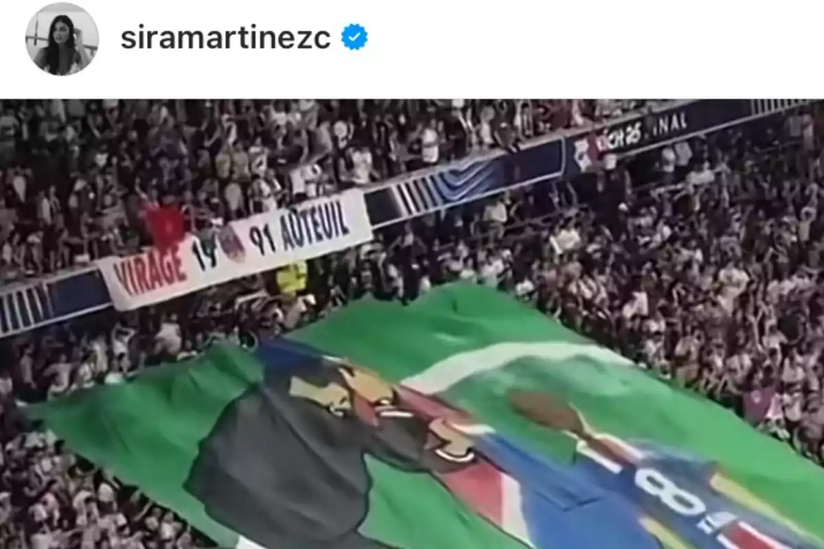 Fans in a stadium unfurl a large banner with a colorful illustration as the crowd watches and cheers from the stands. Fans in a stadium unfurl a large banner with a colorful illustration as the crowd watches and cheers from the stands.
